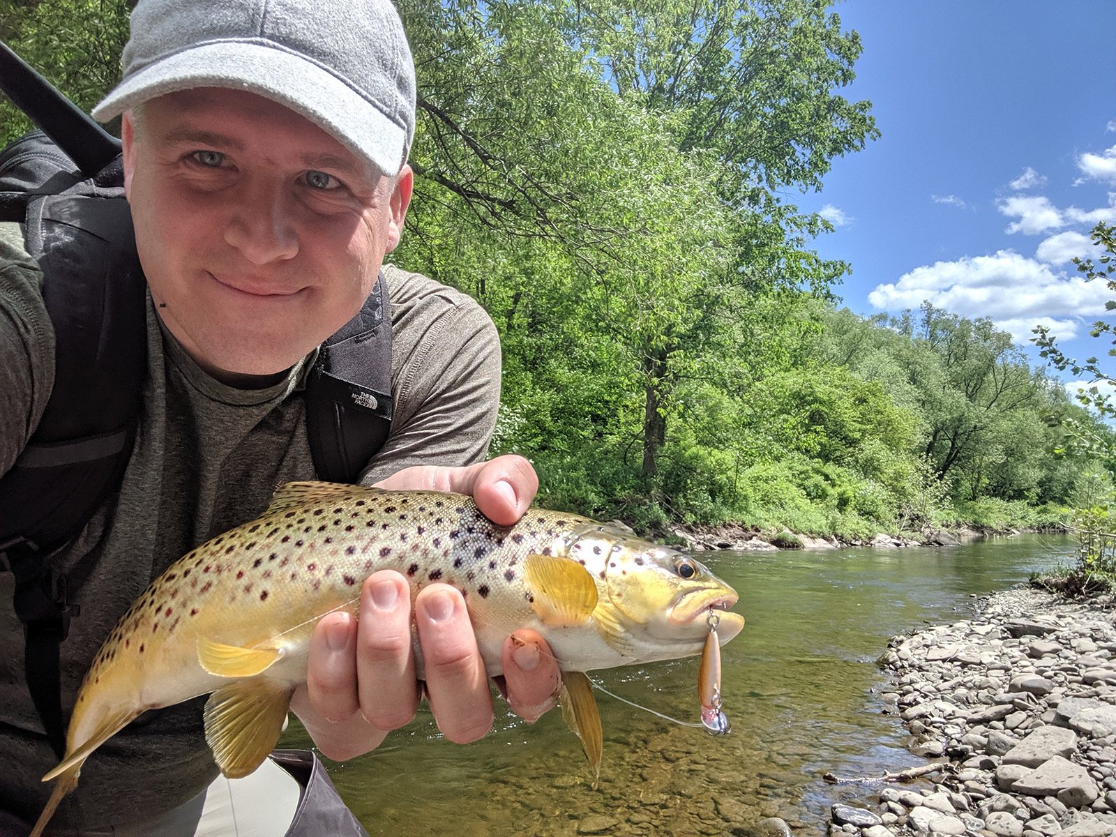 me holding a trout next to a river