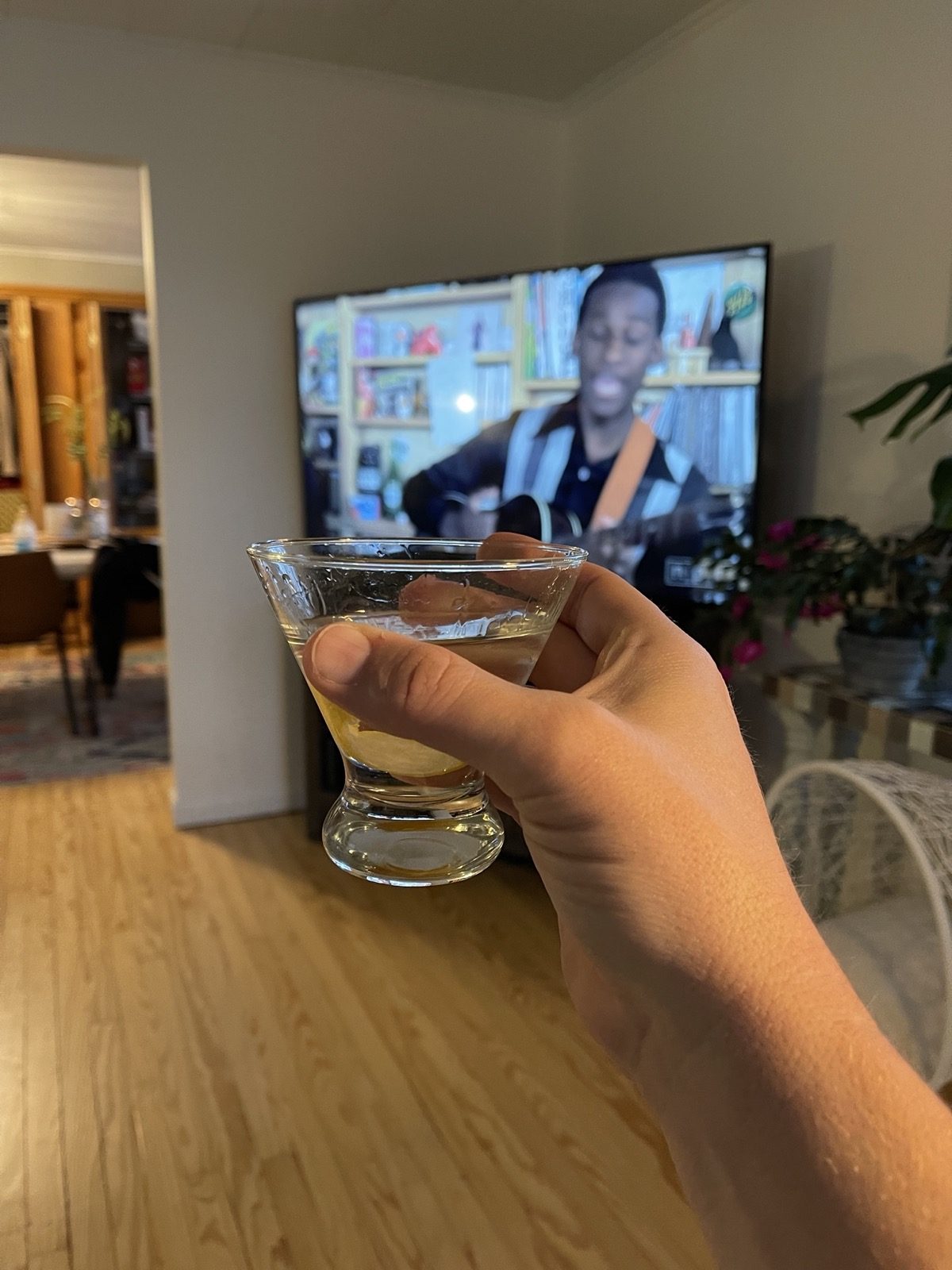 My right hand holding a martini with the TV blurry in the background showing Leon Bridge's tiny desk convert.