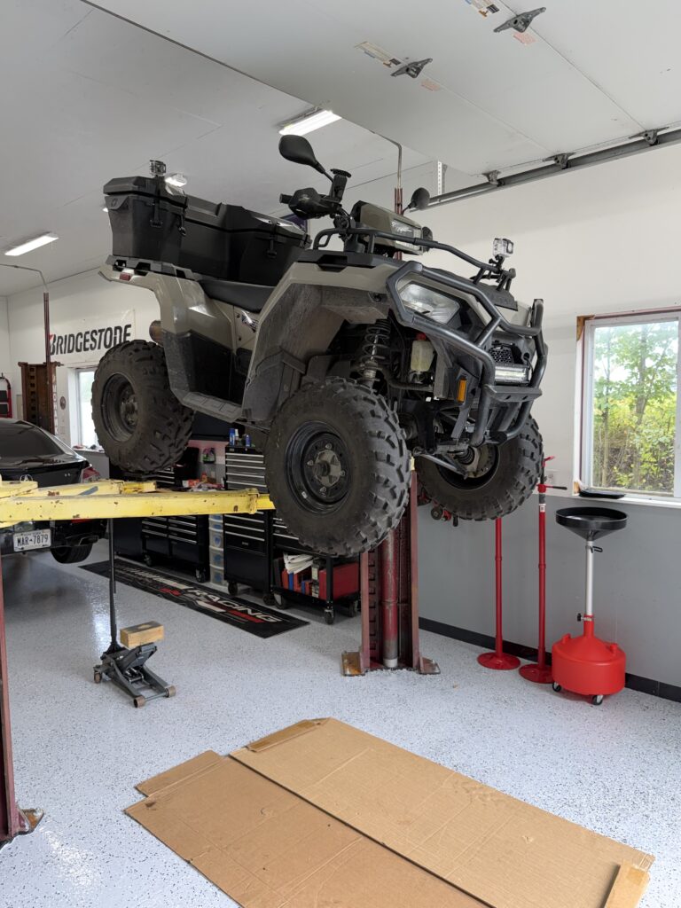 A Polaris Sportsman 570 on a hydraulic lift in a garage.